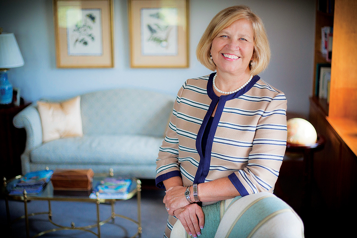 Nursing School dean Linda McCauley  stands next to a desk in a striped suit. A sofa is in the background with two nature prints on the wall above it.