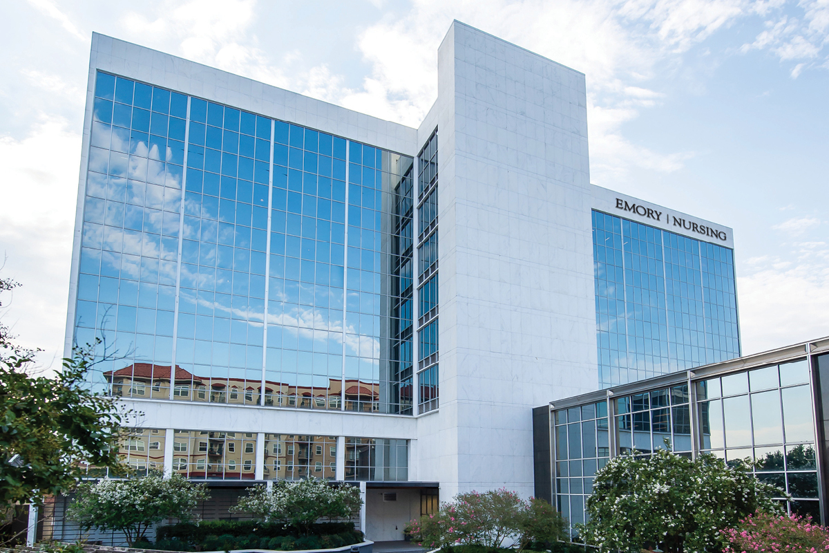 A photo of the exterior of the new Emory Nursing Learning Center. The building is white with large windows reflecting a blue sky with intermittent clouds. The building is surrounded by shrubs and small trees.