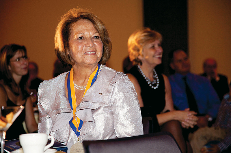 Twilla Haynes in a shimmering white top sits smiling at a table at an event.