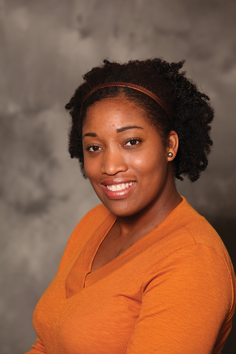 Alexis Dunn wears an orange sweater in a portrait.