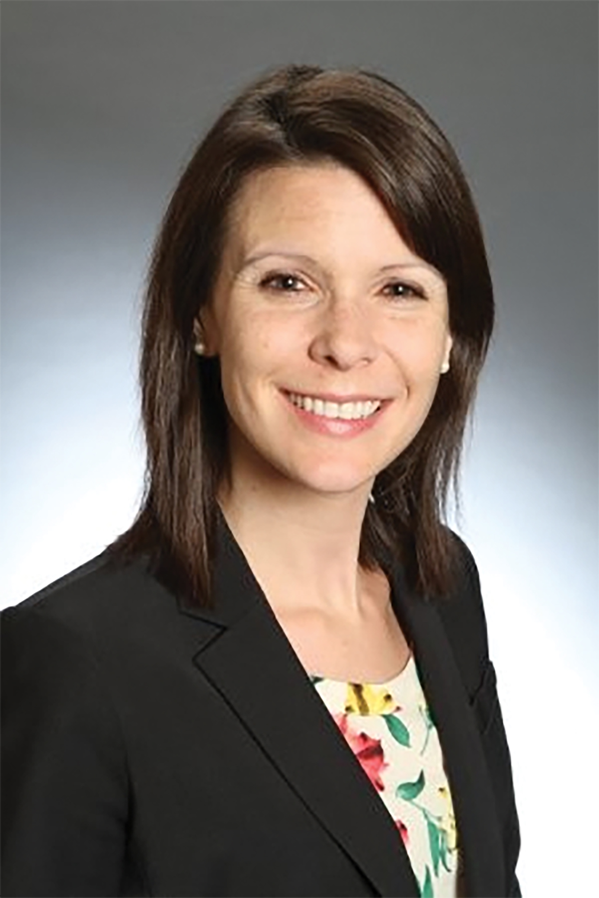 Alison Thompson in a portrait wears a black jacket over a white patterned top while smiling in a portrait.