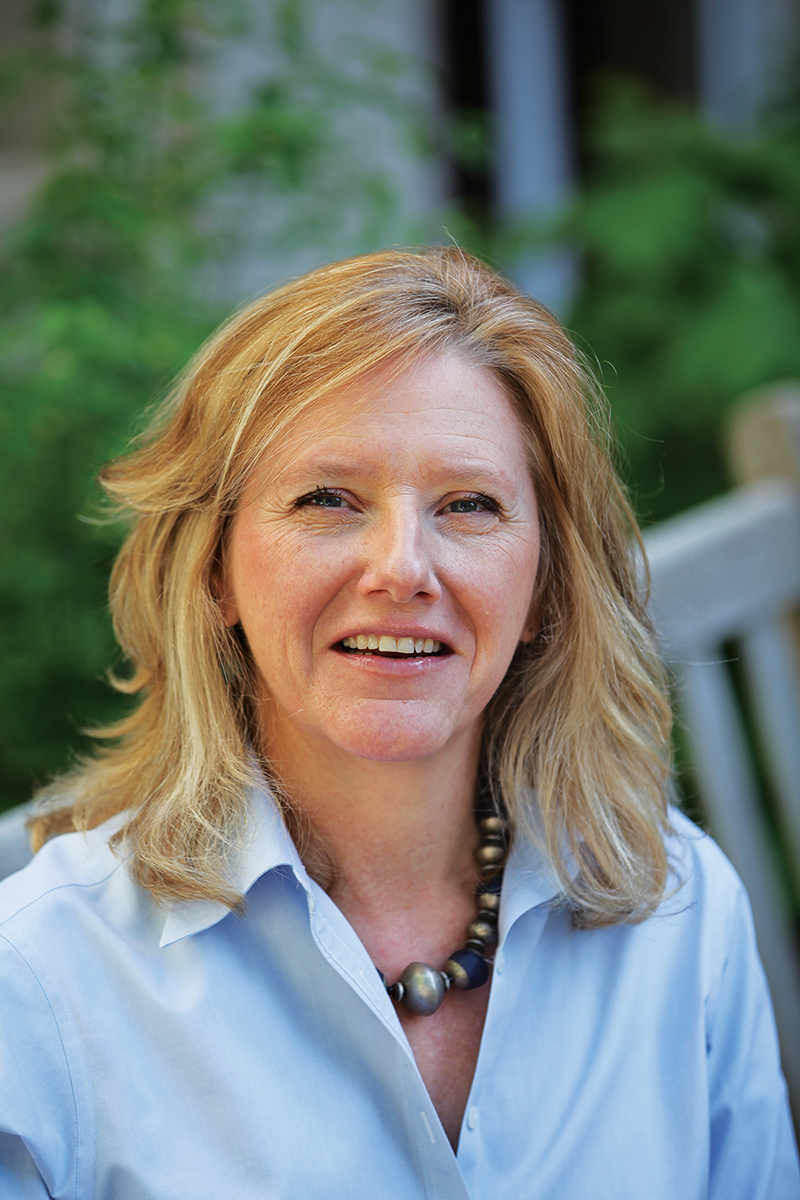 Elizabeth Downes wearing a blue top sits on a bench in an outdoor setting.