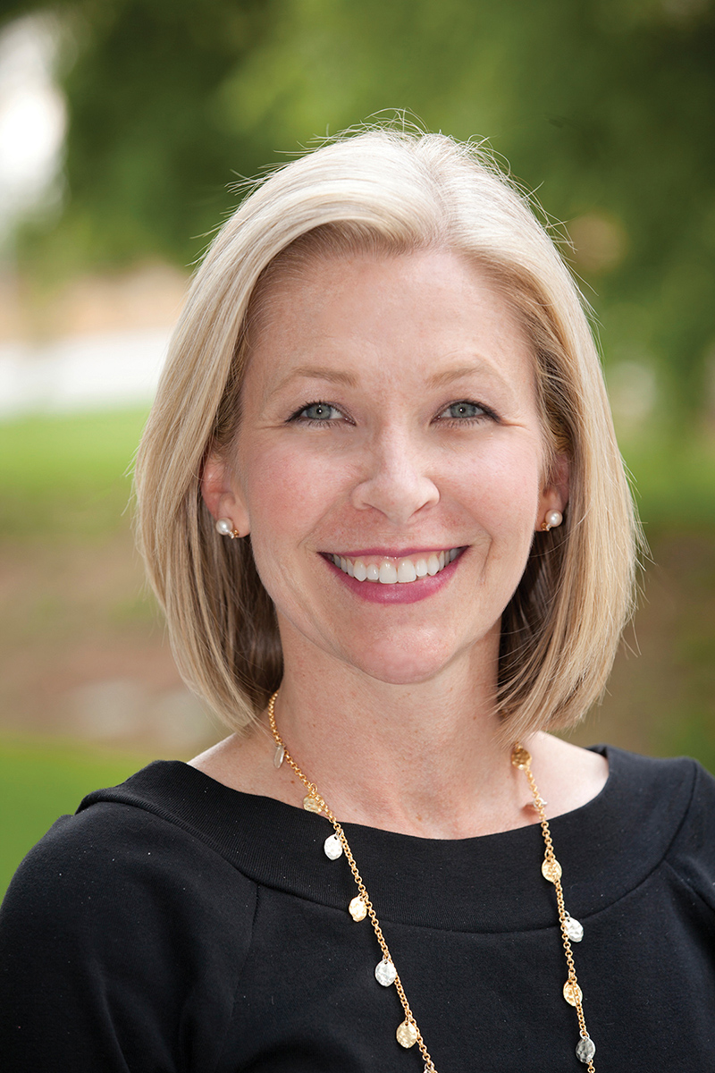 Drenna Waldrop-Valverde wears a black top and gold necklace while smiling in an environmental portrait.